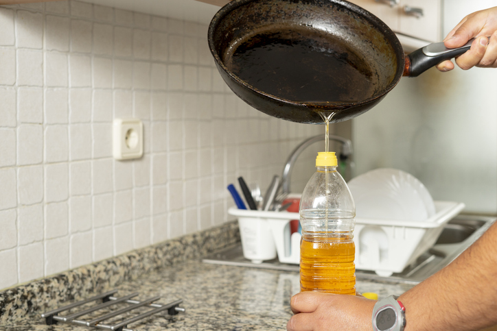 Man placing recycled edible oil from a frying pan into a plastic bottle in his home kitchen. 