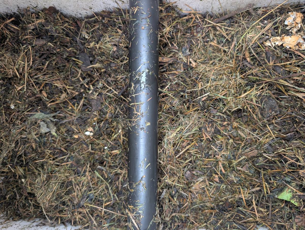 A metal pipe pushed into a compost heap of grass and garden waste