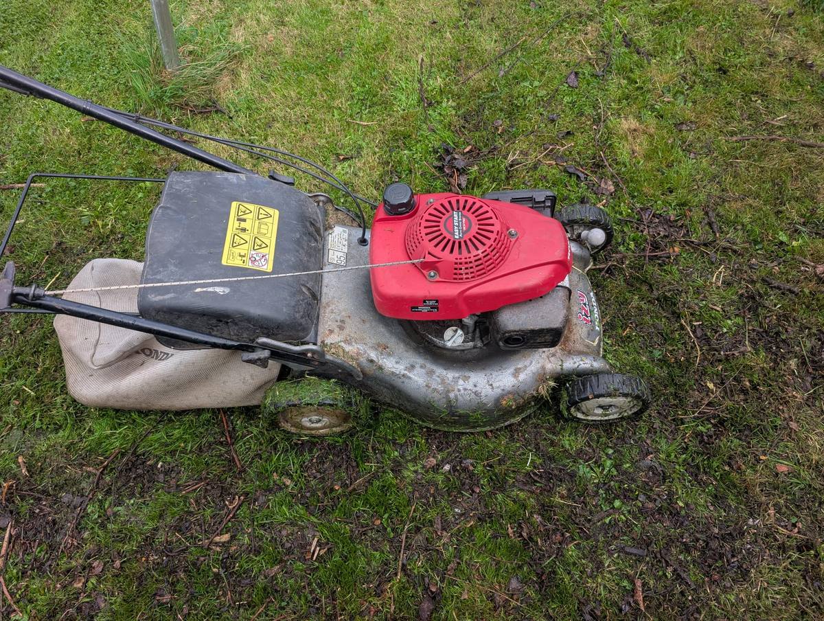 A petrol lawnmower with a grass collection bag on a lawn