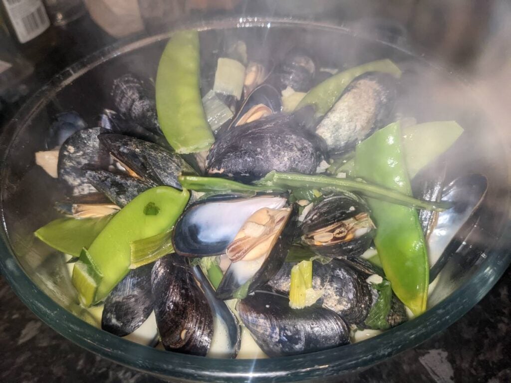 A glass bowl of cooked mussels with mangetout pods
